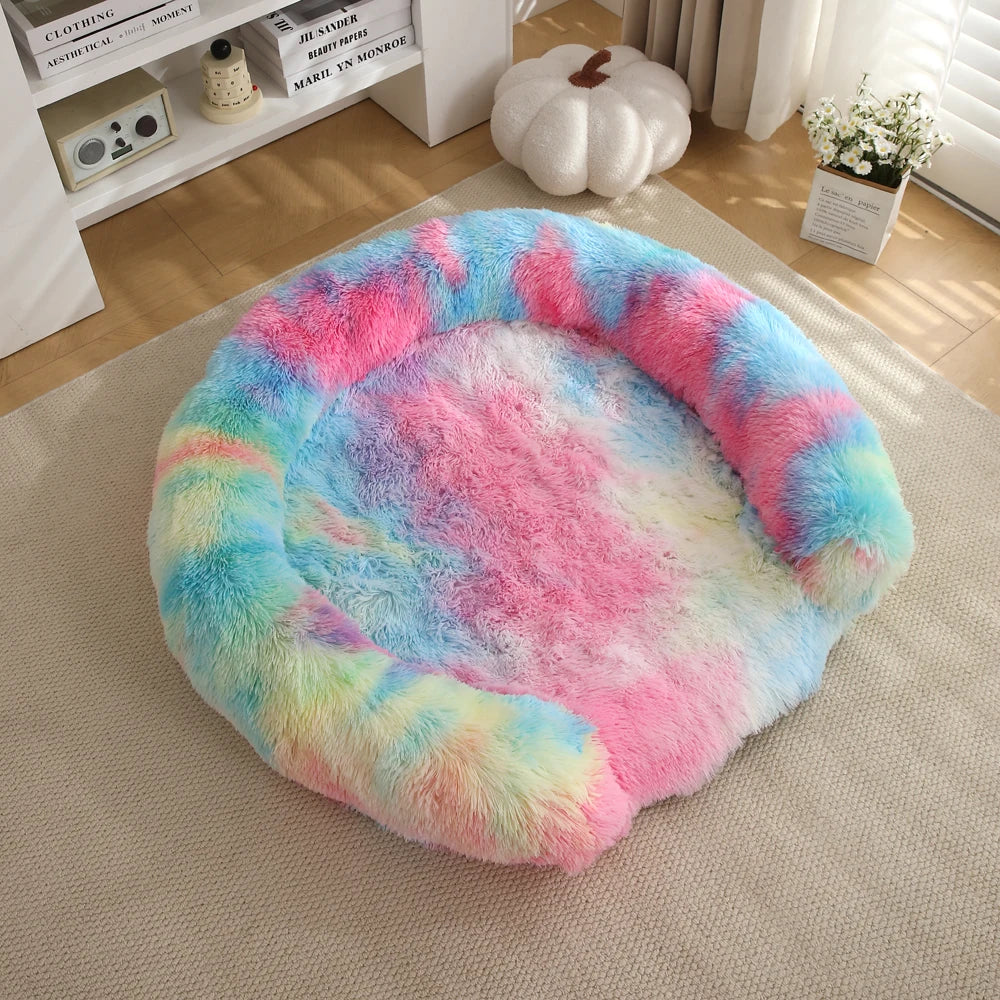 A round, fluffy dog bed with a multicolored pink and blue gradient cover resting on a light beige rug.