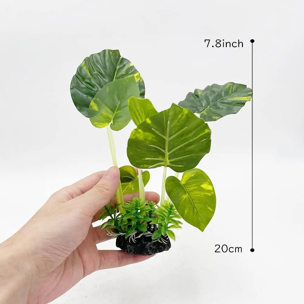 A hand holds a set of realistic plastic plants with secure bases, featuring large green leaves and small foliage.