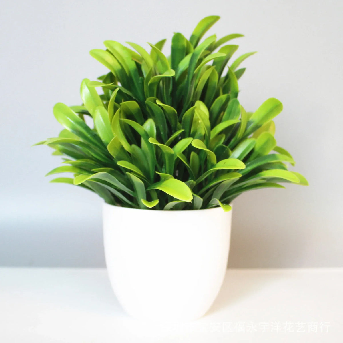A vibrant green artificial bonsai plant in a white pot, displayed indoors.
