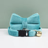 A teal velvet cat collar with a bow knot and a gold safety buckle resting on a white surface.