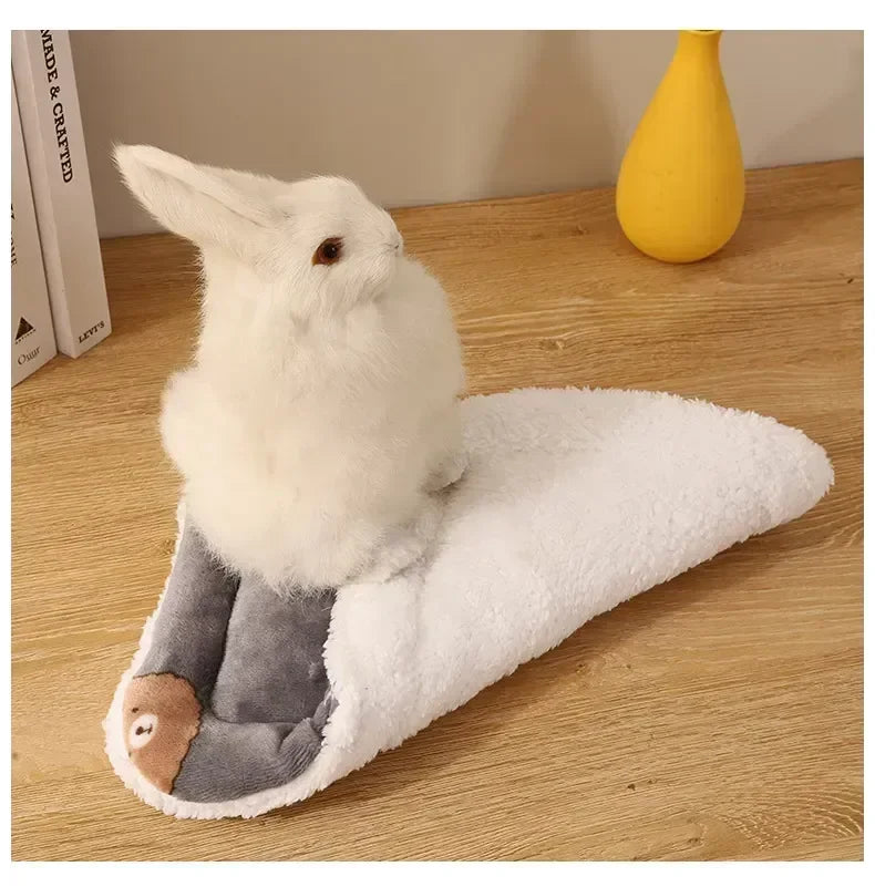 A white fleece pet bed mat for small animals lying on a wooden surface next to a yellow vase.