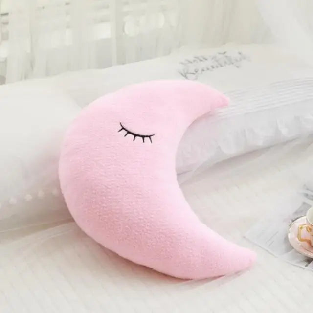 A pink crescent moon shaped plush pillow resting on white bedding.