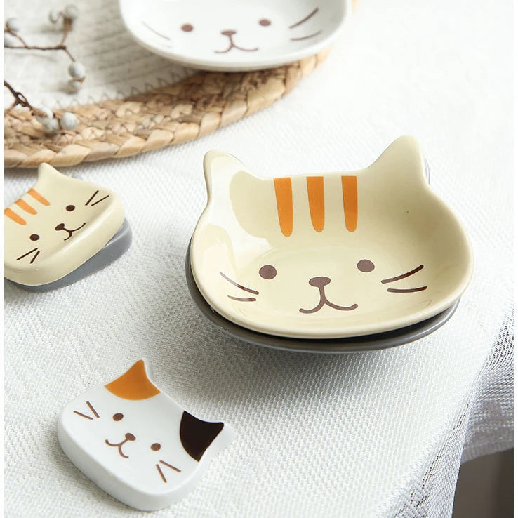 A ceramic cat-shaped sauce dish with orange stripes rests on a white cloth next to a natural fiber mat.