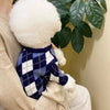 A fluffy white dog toy wearing a navy blue and white plaid knit sweater.