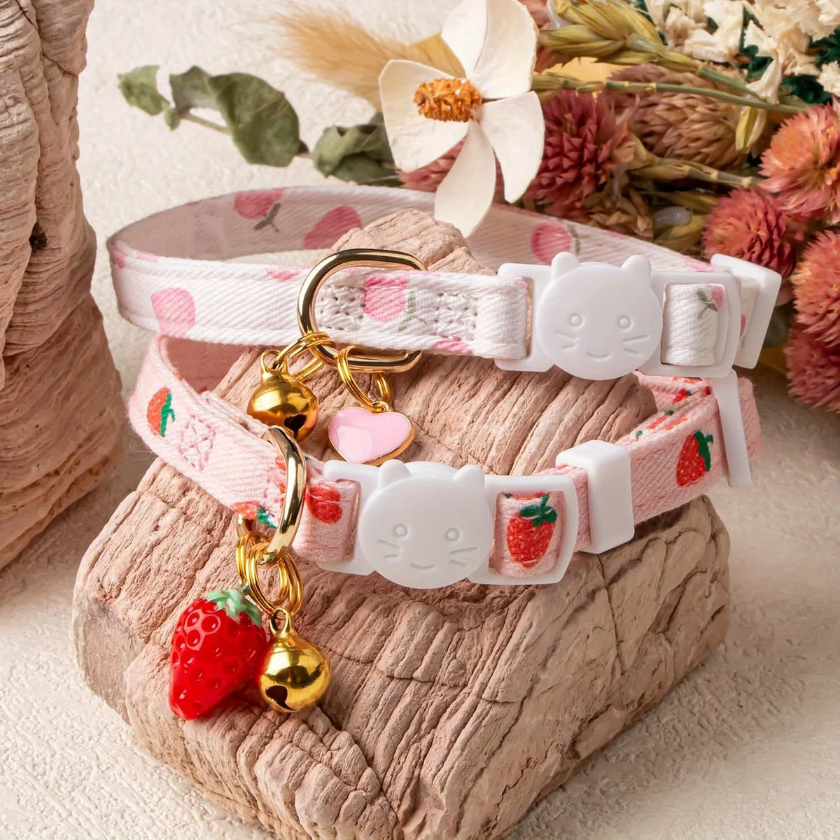 Pink and white cotton breakaway cat collars with strawberry and heart accents displayed on a textured surface.