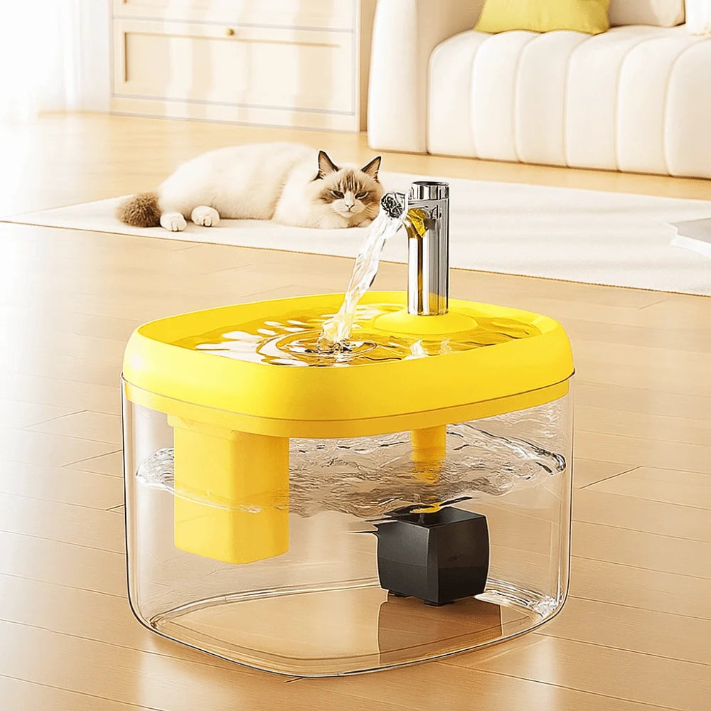 A clear glass pet drinking fountain with a yellow base is shown on a wooden floor, featuring a stream of water.