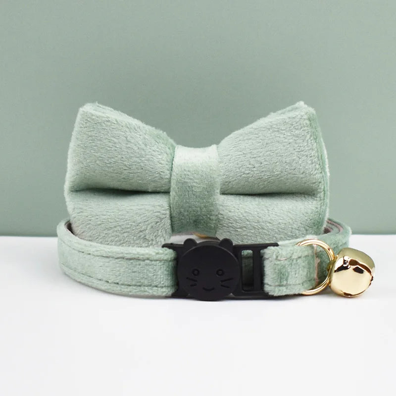 A light mint green velvet cat collar with a bow knot and an adjustable buckle is displayed on a white surface.