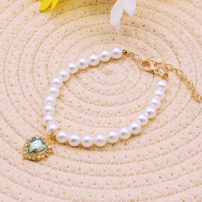 A delicate pearl necklace with a gold chain and an emerald-green gemstone pendant on a beige textured background.