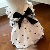 White pet dress with black polka dots and a black bow, displayed on a wooden surface.