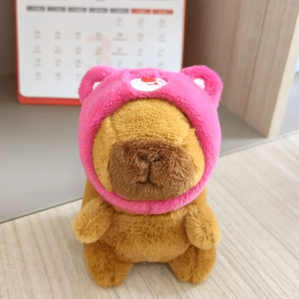Flauschiges braunes Capybara-Plüschtier mit rosa Hoodie und kleinen Flügeln.