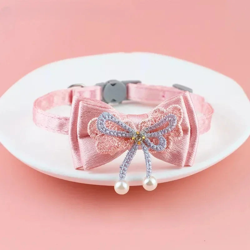 Pink lace bow cat collar with a bell and bead charm displayed on a white plate.