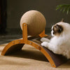 A white cat is relaxing on a wooden scratching board with a round sisal scratching ball.