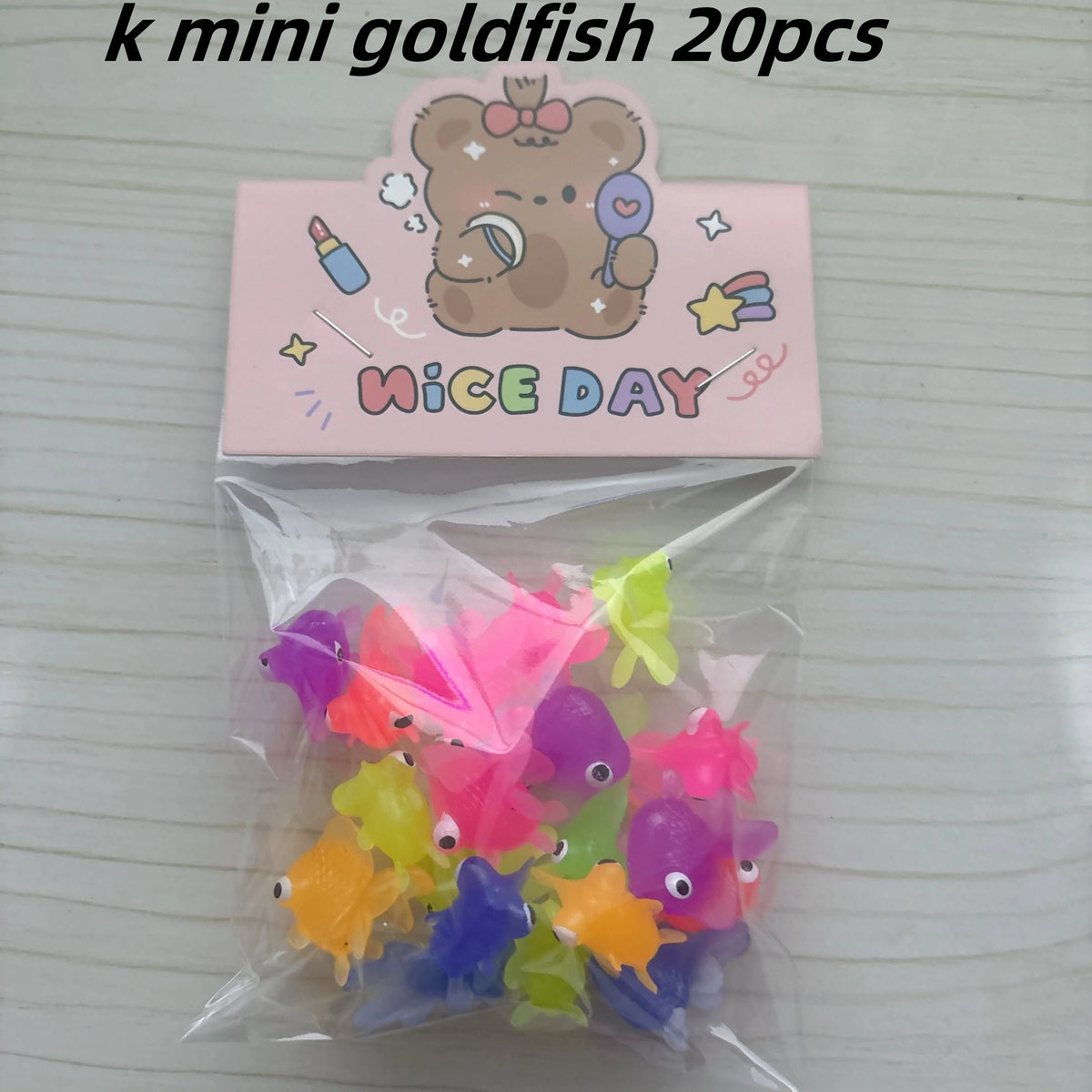 A clear plastic bag contains twenty small, colorful rubber goldfish bath toys with a pink and brown bear design.