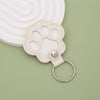 A light beige leather pet paw print keepsake with a silver ring attached, set against a pale green background.