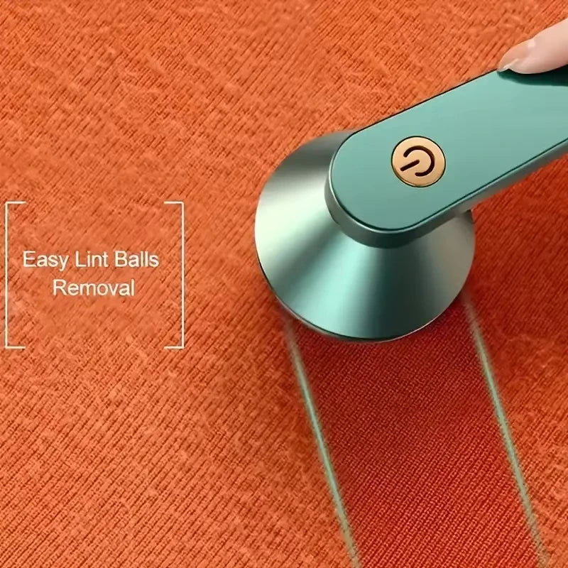 A hand is using a portable electric lint and fabric shaver on an orange surface, demonstrating easy lint ball removal.