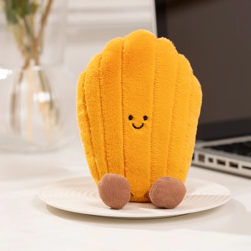 An adorable yellow cactus plush toy with a smiling face sitting on a white plate.