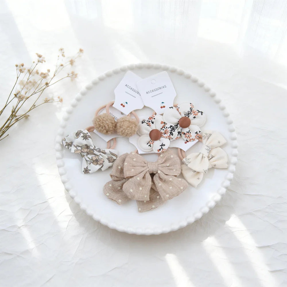 Collection d'attaches pour cheveux élastiques beige et blanc arrangées sur une assiette blanche.