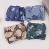 Four reusable dog belly bands in various shades of blue and green laid out on a white surface.