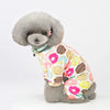 A fluffy gray dog wearing a patterned cotton pajama top with various sweet-themed designs.