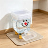A clear plastic pet water fountain with a smiling face is placed on a beige mat.
