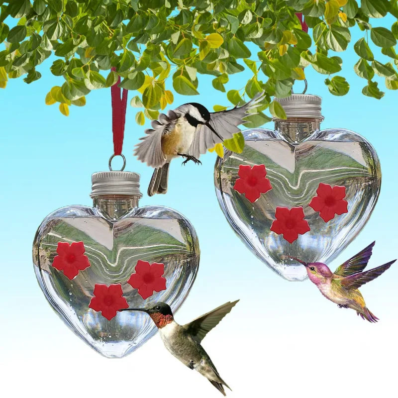 A glass heart-shaped hanging feeder with a hummingbird perched on a green leaf.