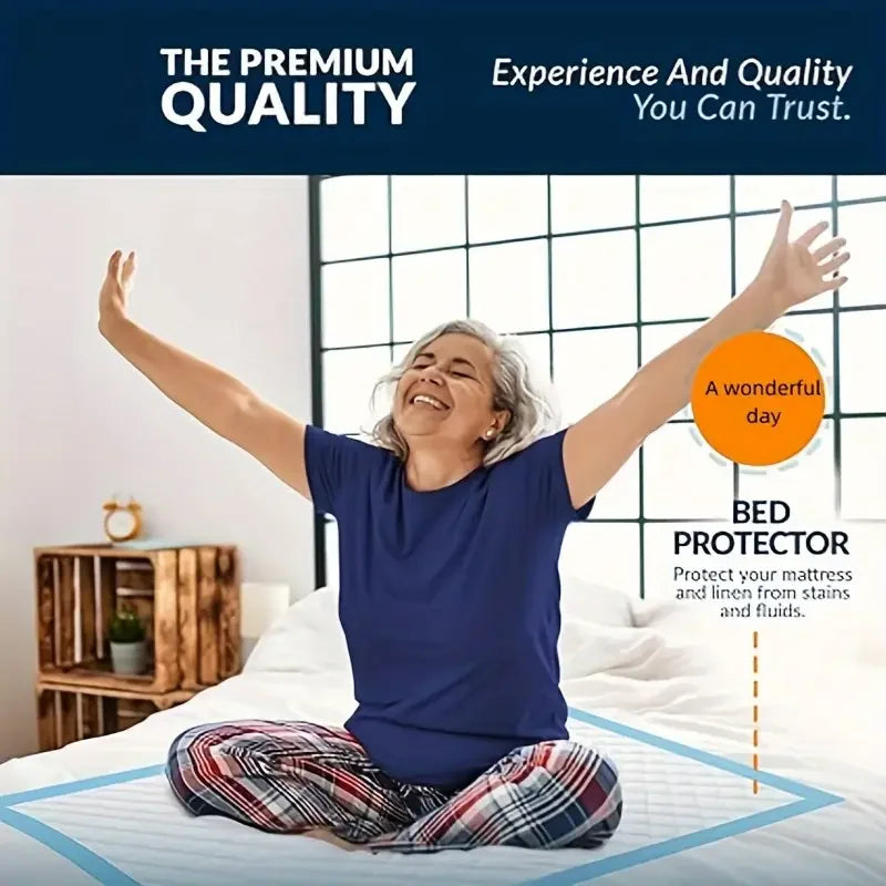 A smiling woman wearing a blue shirt is lying on a bed, demonstrating the use of a bed protector pad.