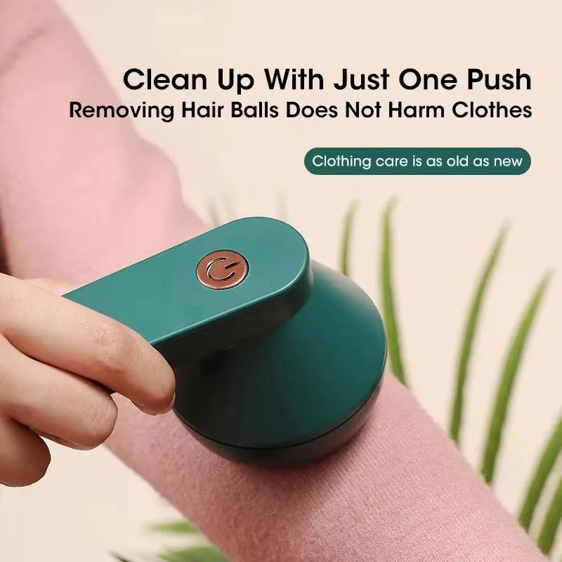 A hand is using a teal portable electric lint and fabric shaver on a pink sleeve, demonstrating its use for cleaning clothes.