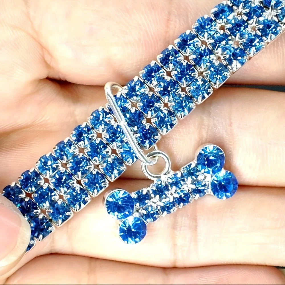 A close-up of a blue gemstone beaded bowknot pet collar being held in a person's hand.