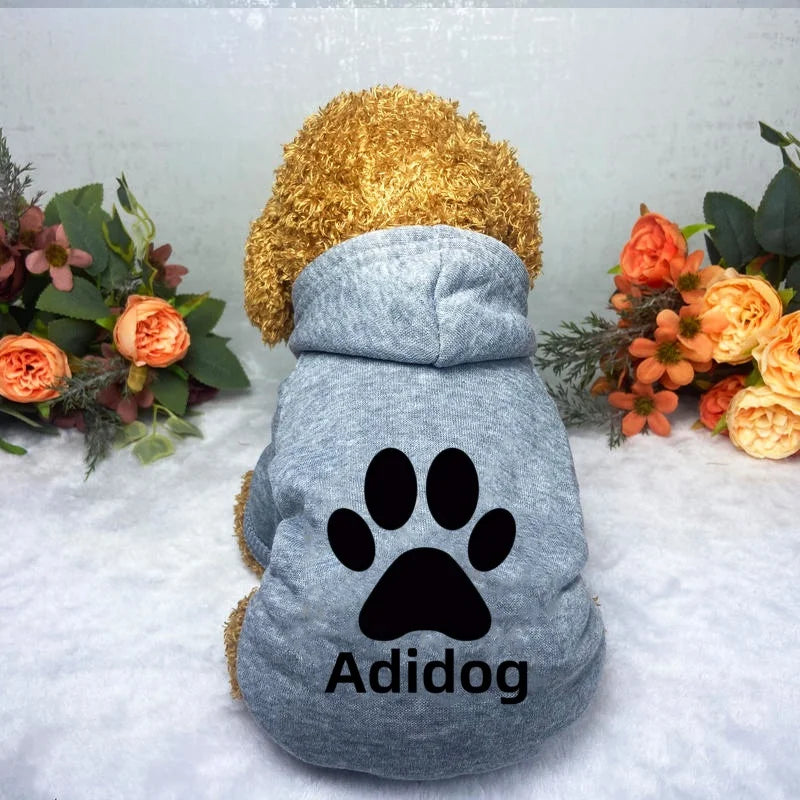 A gray dog hoodie sweatshirt with a black paw print design and a golden fur hood is displayed on a white surface.