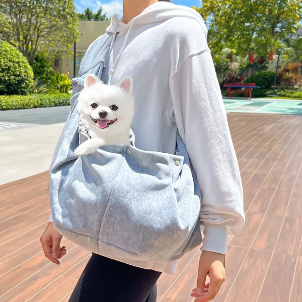 A person is wearing a light gray hands-free pet sling carrier with a small white dog resting inside.