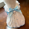 A white dog dress with a light blue heart print and a matching bow, displayed on a wooden surface.