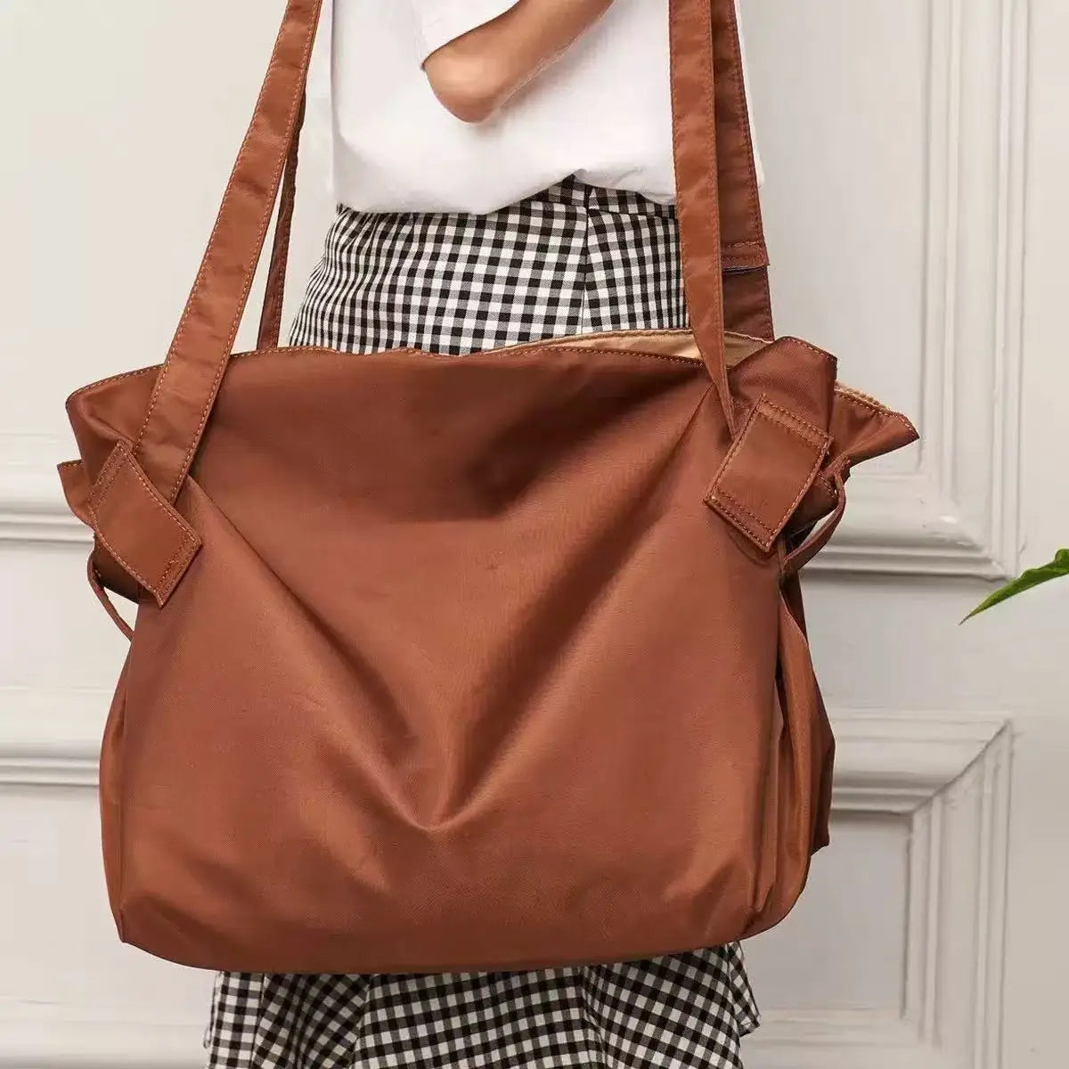 A brown foldable travel organizer bag with a picnic mat carried by a person wearing a checkered skirt.
