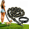 A woman stands next to a large gold-colored chain dog leash and collar lying on green grass.