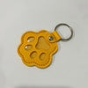A yellow leather pet fur keepsake keychain charm with a rounded shape and multiple holes.