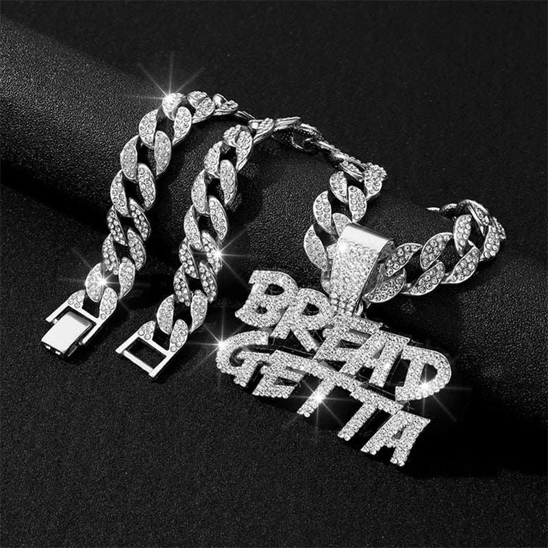 A close-up of an iced out letter and animal pendant Cuban link chain necklace displayed on a black background.