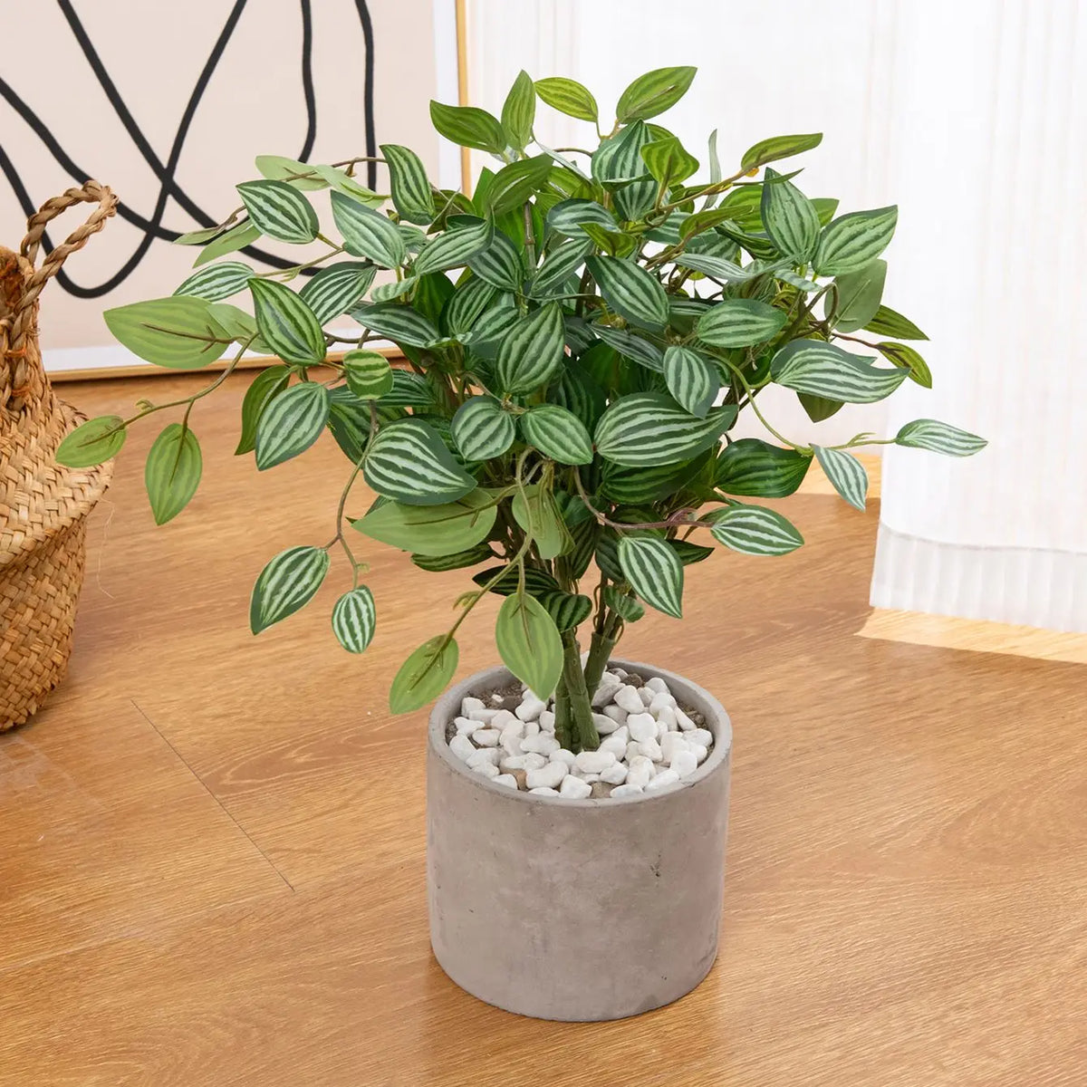 An artificial bonsai tree with green leaves potted in a gray container on a wooden floor.