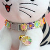 A plush cat toy wearing a rainbow flower collar with a bell.