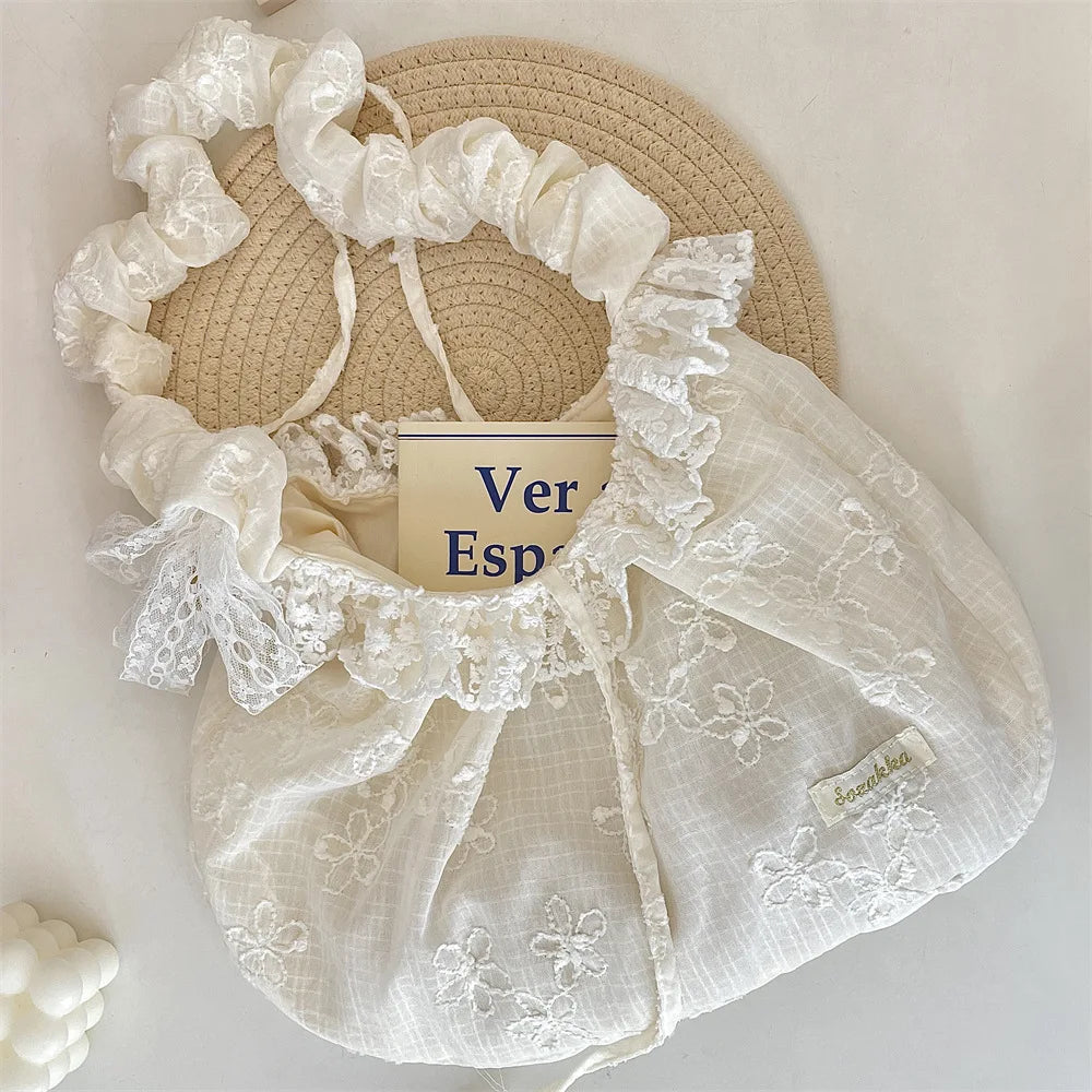 A cream floral lace bowknot shoulder bag with a wide brim straw hat in the background.