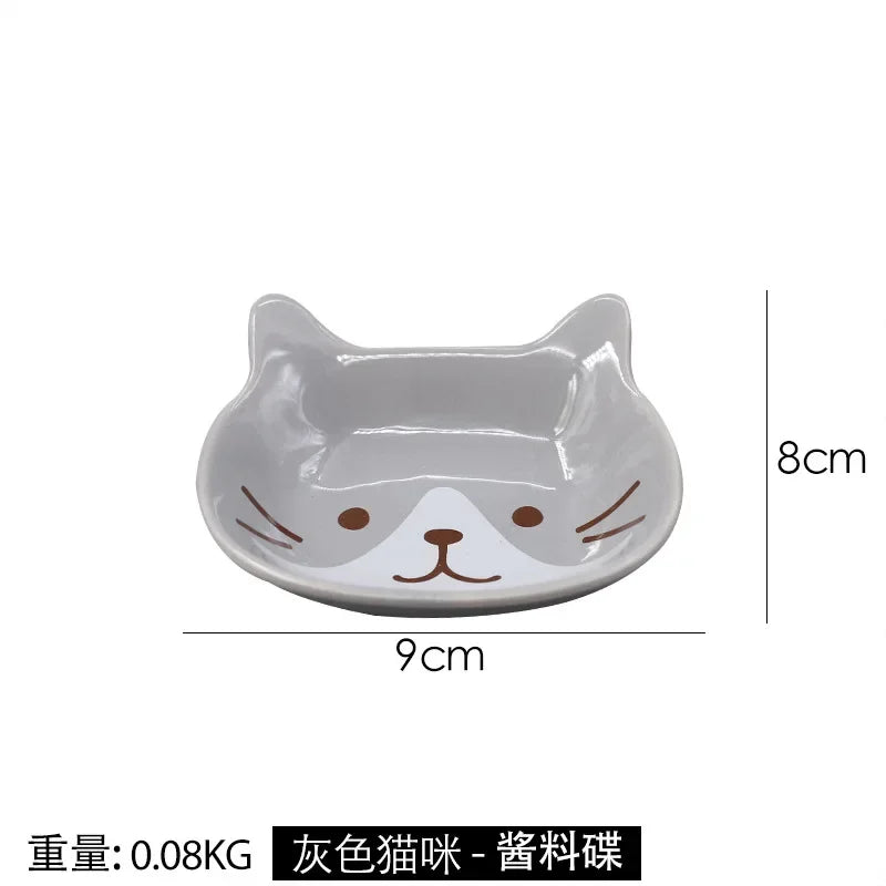 A gray ceramic cat-shaped sauce dish with a white face and brown nose, shown from the top.