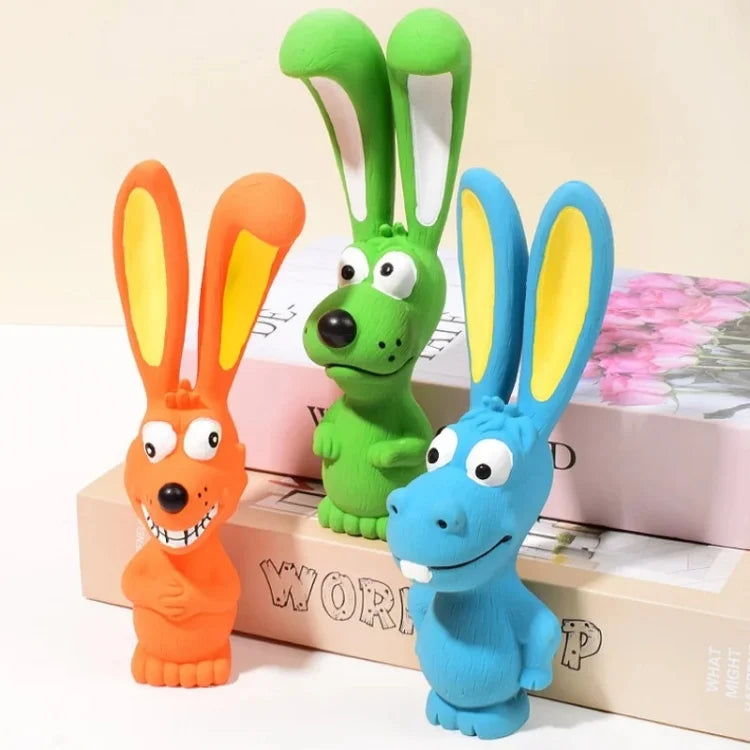 Three rubber squeaky rabbit toys in orange, green, and blue are displayed on a box.