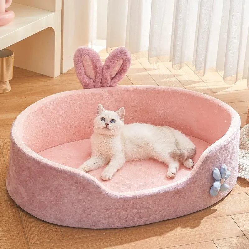 A fluffy white cat is relaxing in a pink plush pet bed with light pink ears.