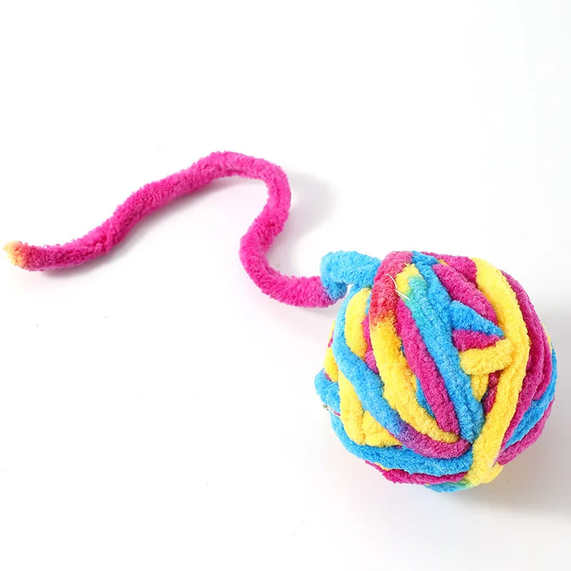 A pink plush cat toy ball with multicolored yarn strands extending from it.