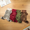 A collection of leopard print dog jumpsuits in various colors laid out on a wooden floor.
