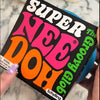 A close-up photo of a black stress ball labeled SUPER NEE DOH in bright pink and orange text, held by a hand.