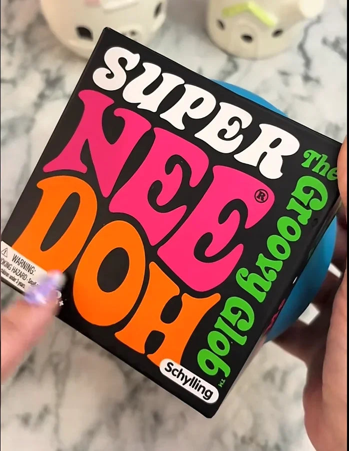 A close-up photo of a black stress ball labeled SUPER NEE DOH in bright pink and orange text, held by a hand.