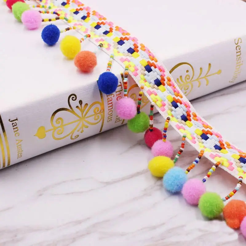 Lace trim featuring colorful mini pom poms in various shades of pink, yellow, and orange for sewing and crafts