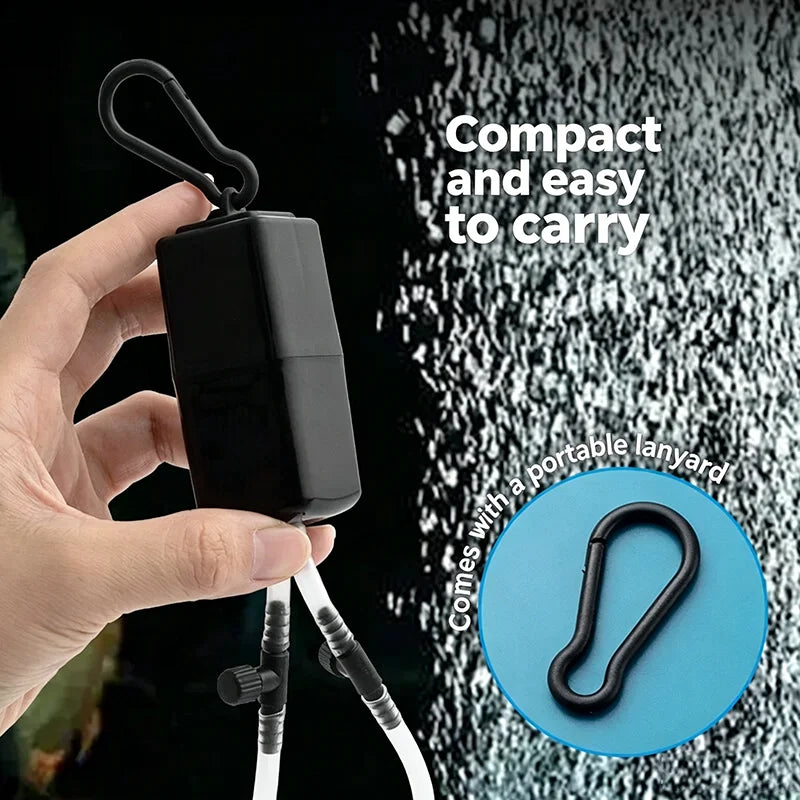 A hand holds a compact black USB aquarium air pump with an adjustable flow and air stone, featuring a portable lanyard.
