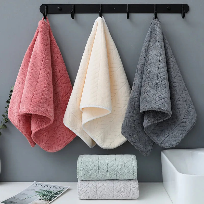 Three folded gray and pink bath towels are hanging on a rack above stacked white towels.