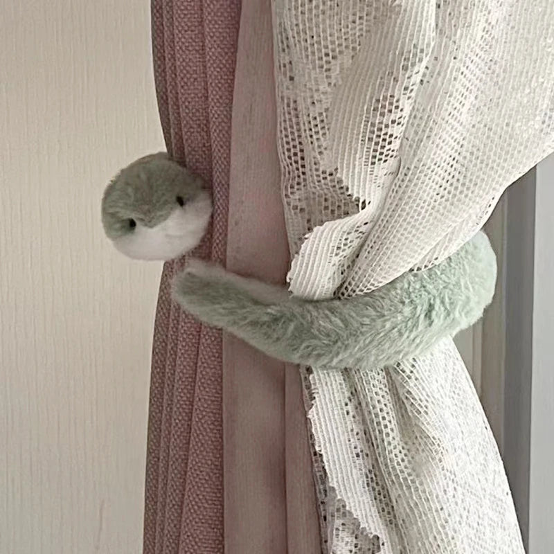 A small, soft, light green snake plush toy is hanging from a pink curtain.
