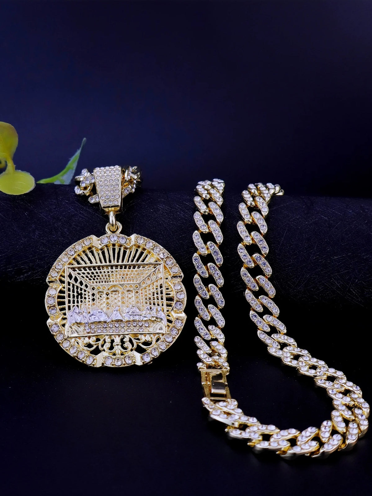 A gold plated last supper medallion pendant on a chain next to a Cuban link necklace.
